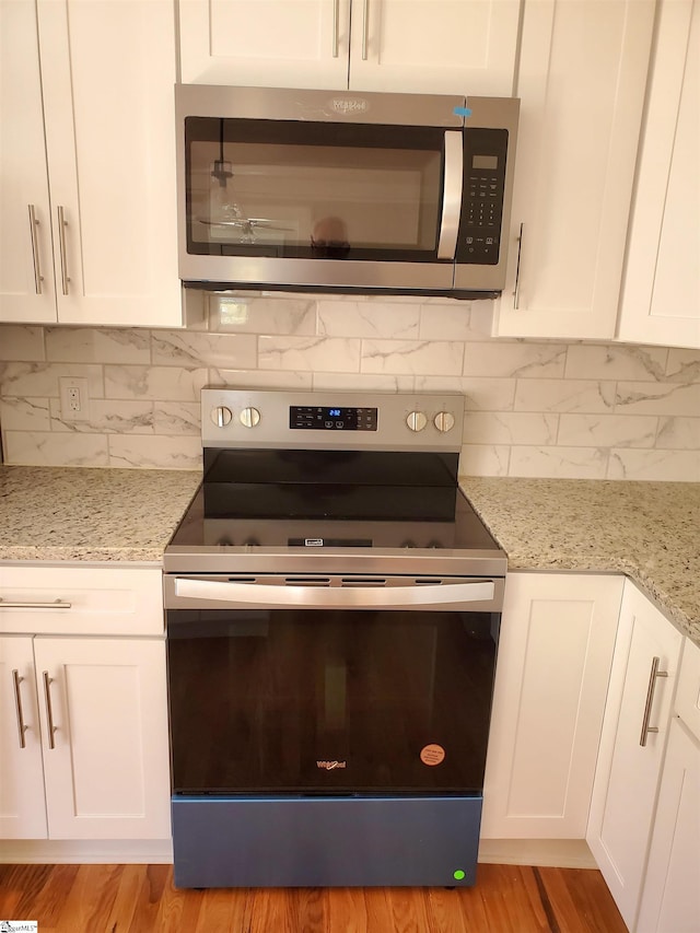 kitchen with stainless steel appliances, light stone counters, decorative backsplash, and white cabinets