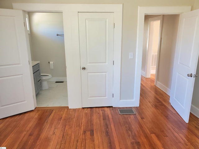 unfurnished bedroom featuring wood-type flooring, connected bathroom, visible vents, and baseboards