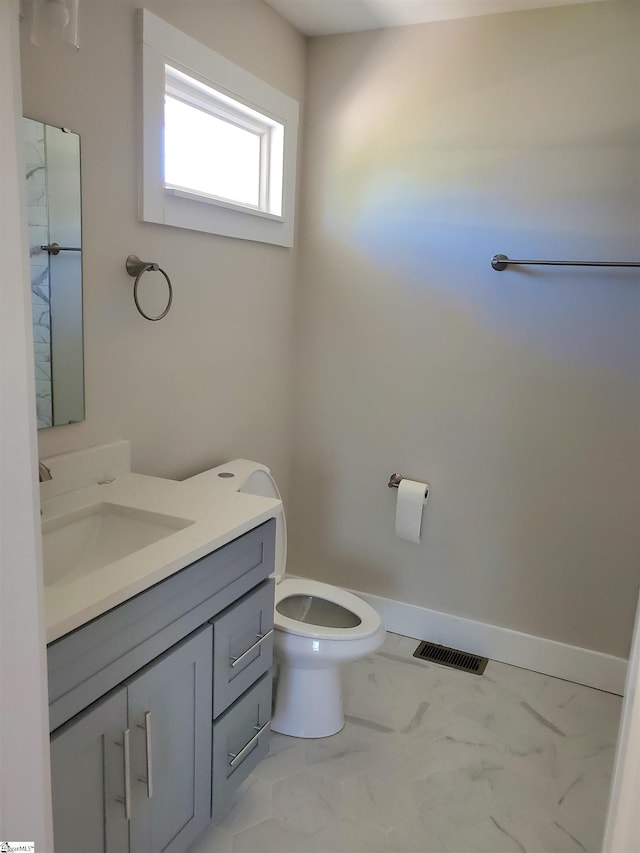 half bathroom with marble finish floor, visible vents, toilet, vanity, and baseboards