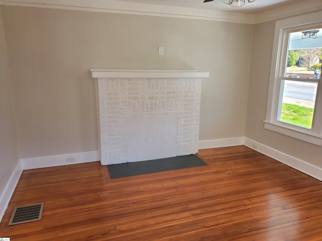 unfurnished living room featuring wood-type flooring, visible vents, ornamental molding, a fireplace with flush hearth, and baseboards