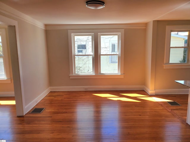 empty room featuring plenty of natural light, visible vents, and wood finished floors