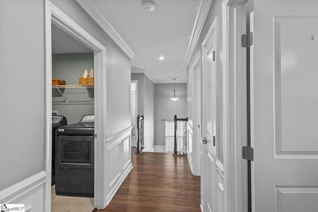 corridor featuring a decorative wall, ornamental molding, washing machine and dryer, an upstairs landing, and wood finished floors