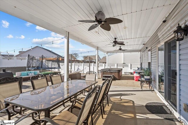 view of patio featuring a trampoline, a hot tub, outdoor dining space, ceiling fan, and a fenced backyard