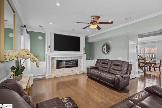 living area with a glass covered fireplace, visible vents, crown molding, and wood finished floors