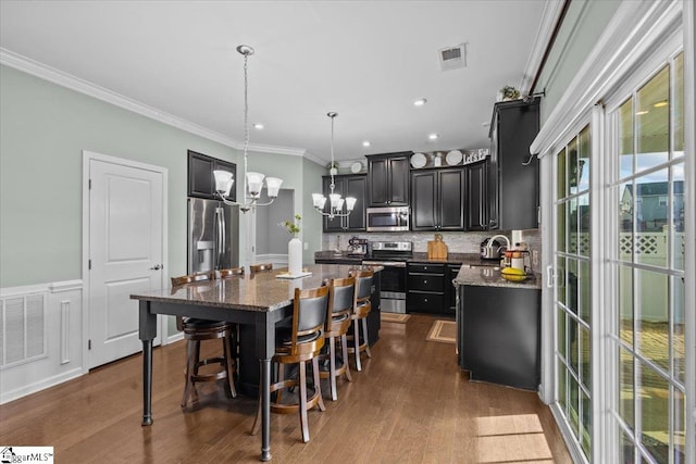 kitchen with visible vents, a kitchen island, ornamental molding, stainless steel appliances, and dark cabinetry