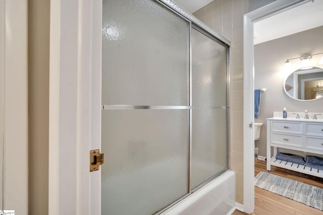 bathroom with toilet, bath / shower combo with glass door, wood finished floors, and vanity