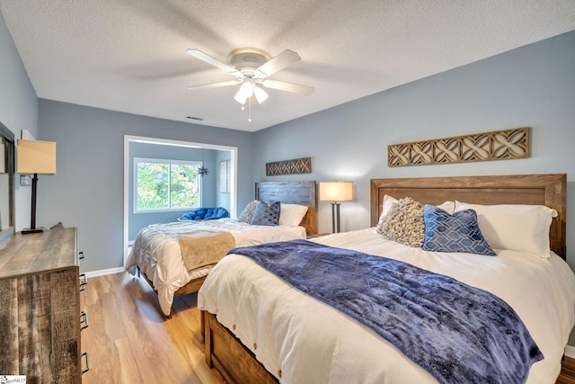 bedroom featuring visible vents, baseboards, ceiling fan, wood finished floors, and a textured ceiling