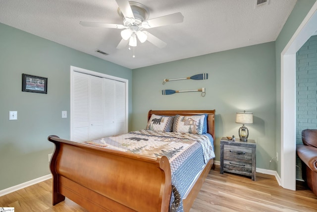 bedroom featuring light wood finished floors, baseboards, visible vents, a textured ceiling, and a closet