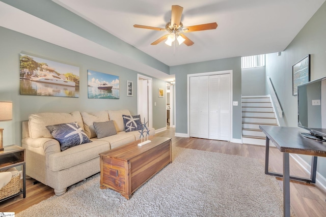 living area with a ceiling fan, stairway, baseboards, and wood finished floors