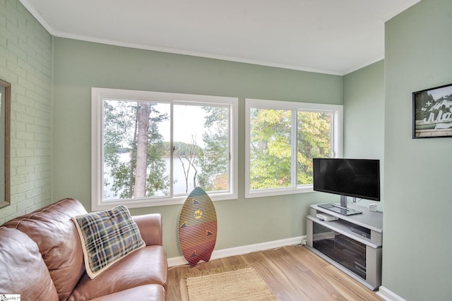 living area featuring brick wall, baseboards, crown molding, and light wood finished floors