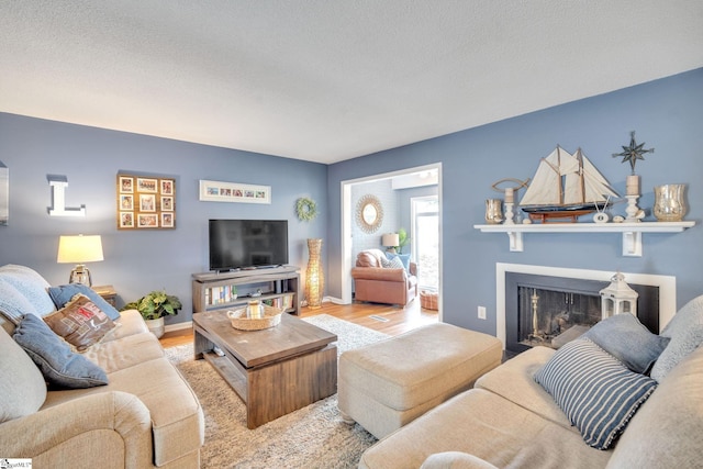 living room with a fireplace, a textured ceiling, baseboards, and wood finished floors