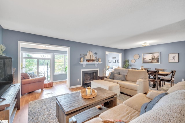 living room featuring light wood-style floors, a fireplace with flush hearth, and baseboards