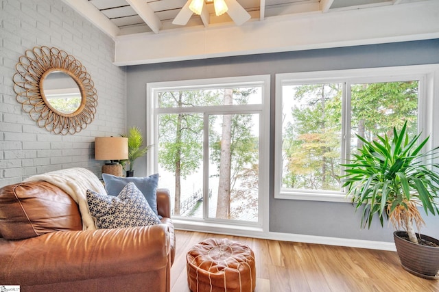 living area featuring brick wall, beamed ceiling, wood finished floors, and baseboards