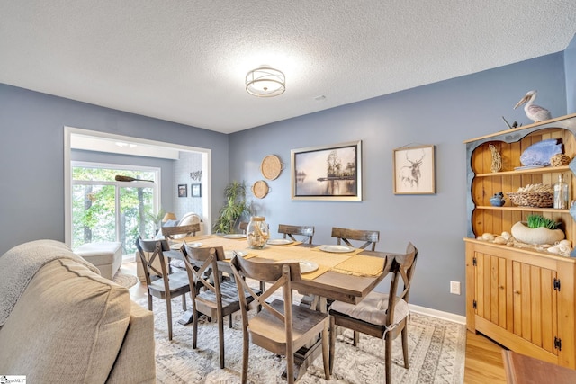 dining space with light wood-style flooring, baseboards, and a textured ceiling