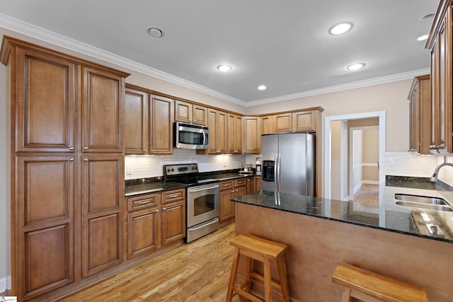 kitchen featuring a peninsula, a sink, appliances with stainless steel finishes, light wood-type flooring, and dark stone countertops