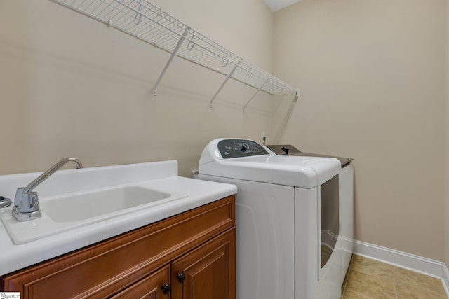 washroom featuring cabinet space, light tile patterned floors, baseboards, washer and clothes dryer, and a sink