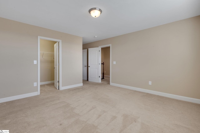 unfurnished bedroom with light carpet, a spacious closet, baseboards, and a closet