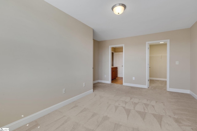 unfurnished bedroom with a closet, light carpet, a spacious closet, and baseboards