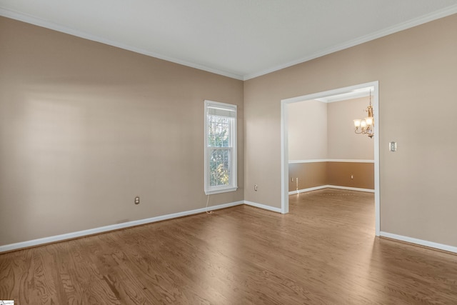 empty room featuring a notable chandelier, baseboards, wood finished floors, and ornamental molding