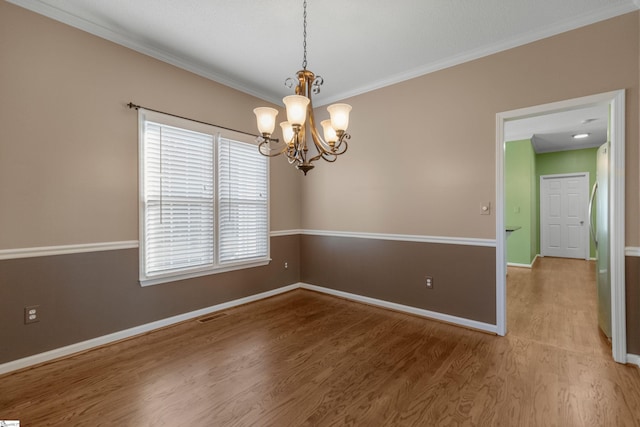 empty room with baseboards, visible vents, ornamental molding, wood finished floors, and a chandelier