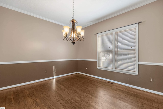 spare room featuring a notable chandelier, wood finished floors, visible vents, baseboards, and ornamental molding