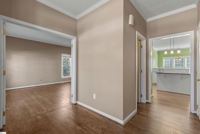 hallway with a sink, baseboards, ornamental molding, and wood finished floors