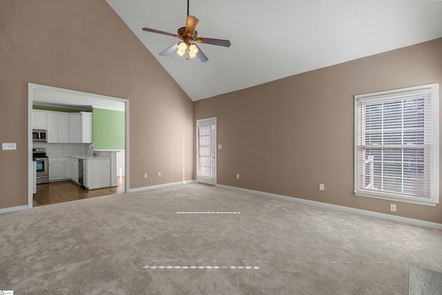 unfurnished living room featuring a sink, plenty of natural light, high vaulted ceiling, and carpet flooring