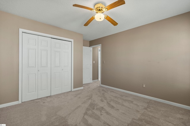 unfurnished bedroom featuring a textured ceiling, baseboards, a closet, and light colored carpet