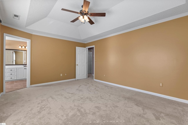 unfurnished bedroom with light carpet, baseboards, a raised ceiling, ensuite bath, and ornamental molding