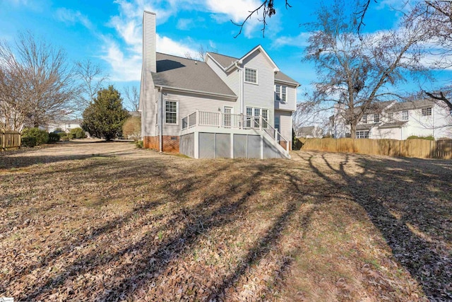 rear view of property featuring fence, stairs, a lawn, a wooden deck, and a chimney