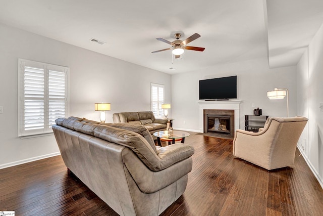 living area featuring dark wood-type flooring, a fireplace with flush hearth, visible vents, and baseboards