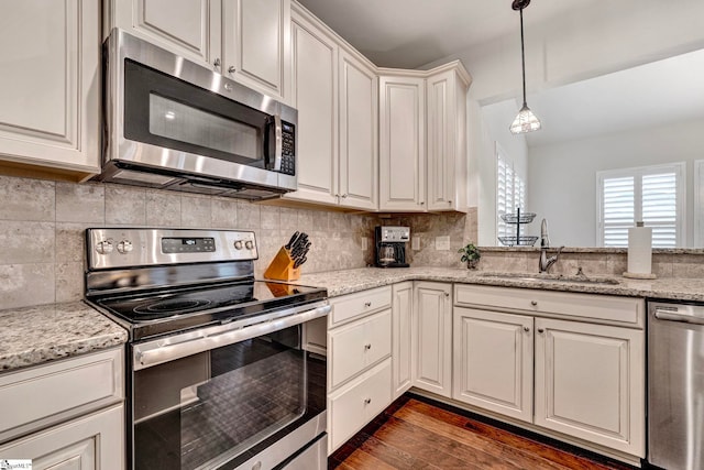 kitchen with stainless steel appliances, dark wood-style flooring, a sink, backsplash, and pendant lighting