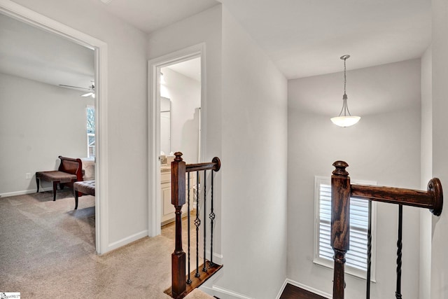 corridor with baseboards, light colored carpet, and an upstairs landing