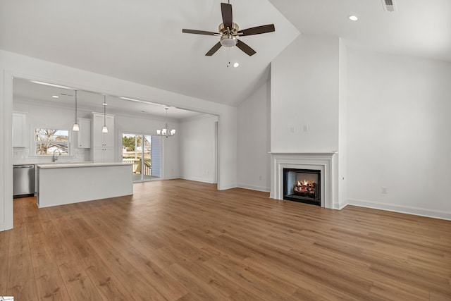 unfurnished living room featuring baseboards, light wood-style flooring, a lit fireplace, a sink, and ceiling fan with notable chandelier