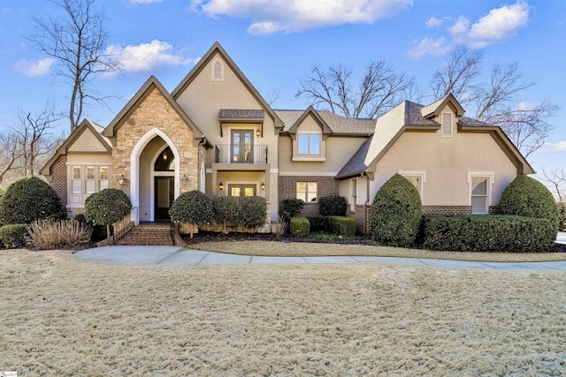 view of front of home featuring a balcony, brick siding, stone siding, french doors, and stucco siding