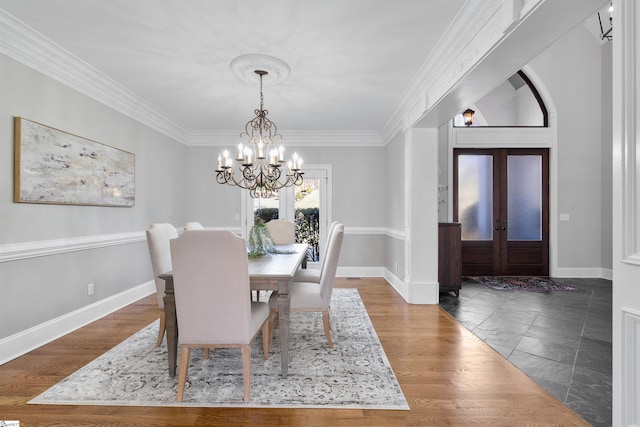 dining space with baseboards, wood finished floors, an inviting chandelier, crown molding, and french doors