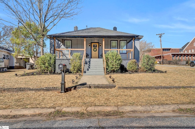 bungalow with covered porch, a shingled roof, a chimney, and stucco siding