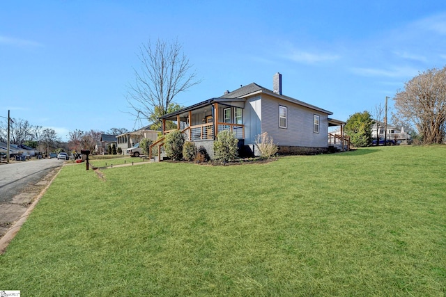 view of side of home featuring covered porch, a chimney, and a yard