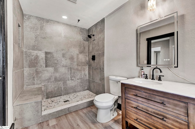 full bath with a textured wall, toilet, wood finished floors, a tile shower, and vanity