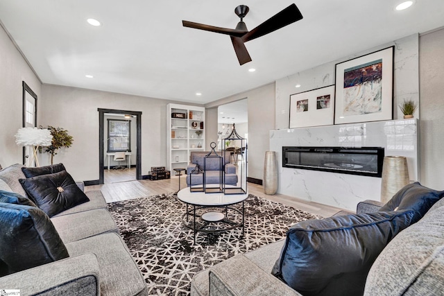 living area featuring recessed lighting, a high end fireplace, ceiling fan, wood finished floors, and baseboards