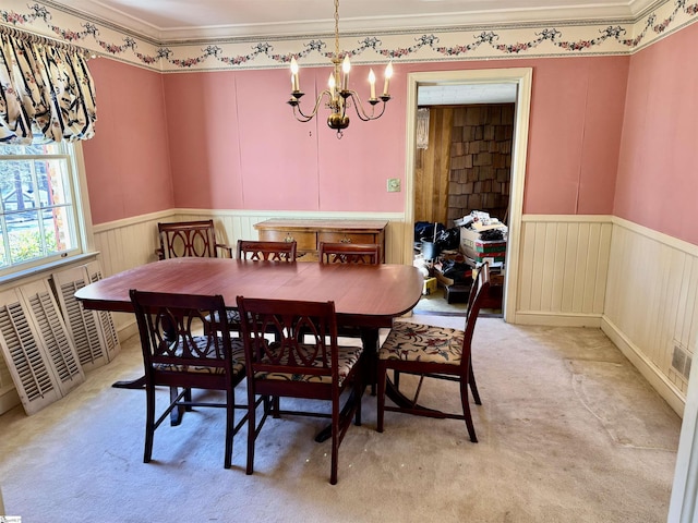 dining space with a wainscoted wall, ornamental molding, an inviting chandelier, and light colored carpet