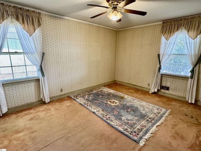 unfurnished room with carpet floors, a ceiling fan, baseboards, wallpapered walls, and crown molding