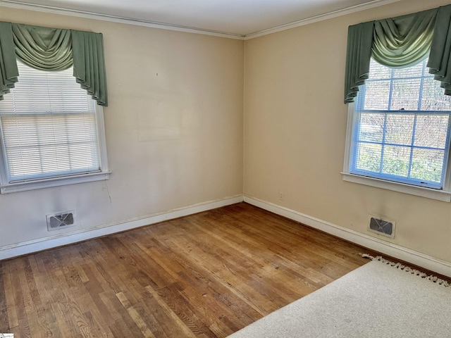 spare room with wood finished floors, visible vents, and crown molding