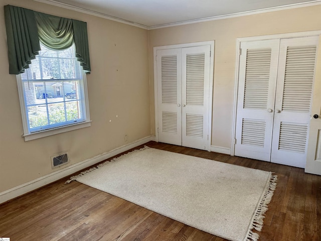 unfurnished bedroom with ornamental molding, french doors, dark wood-style flooring, and two closets