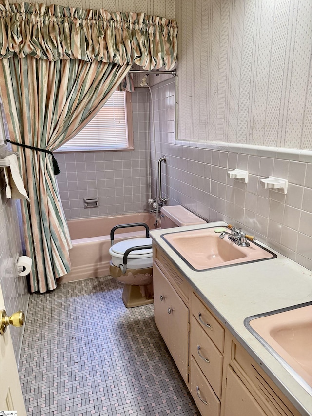 bathroom with toilet, double vanity, a sink, and tile walls