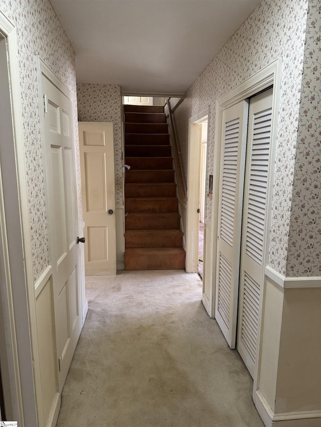 hall featuring light carpet, stairs, and wallpapered walls