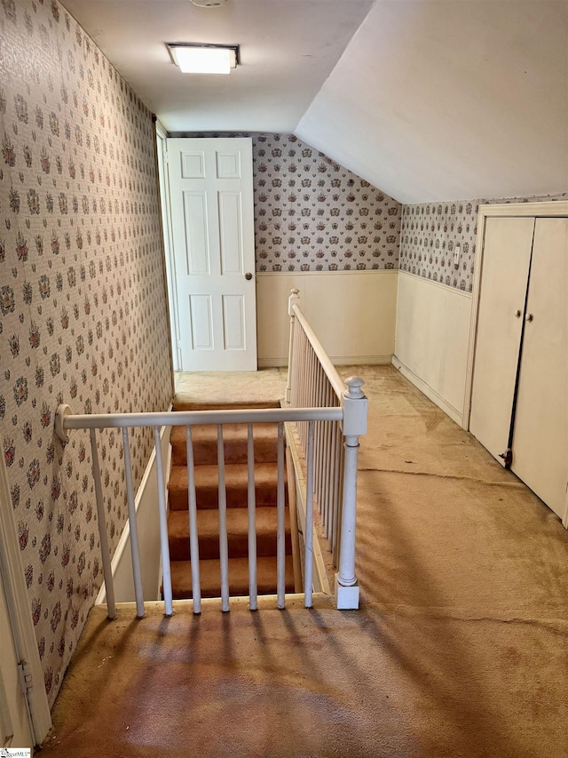 hall featuring vaulted ceiling, an upstairs landing, and wallpapered walls