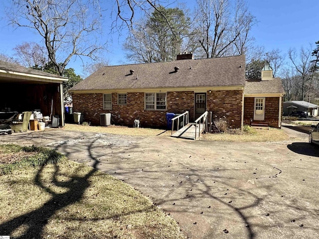 back of house featuring brick siding, roof with shingles, a chimney, and central AC unit