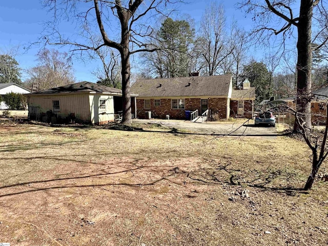 rear view of property with brick siding, a chimney, and an outdoor structure