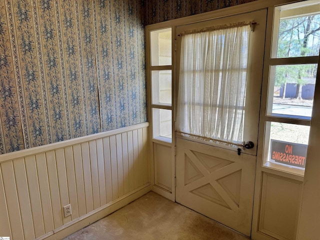 doorway featuring a wainscoted wall, light colored carpet, and wallpapered walls